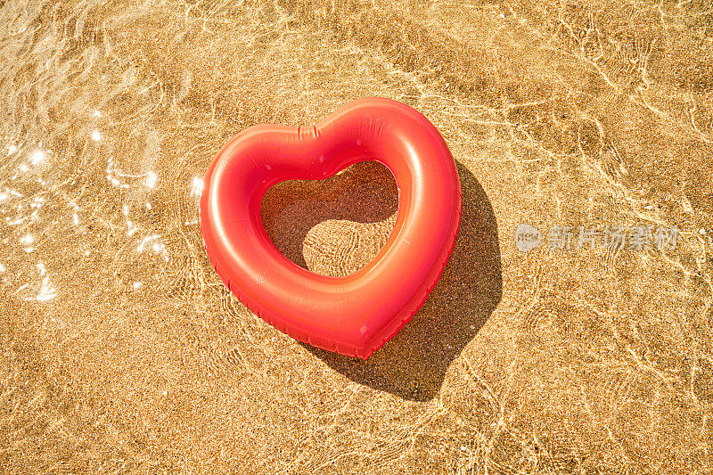 夏天的一天，康沃尔的Pedn Vounder海滩，红心形的橡胶圈漂浮在波光粼粼的浅海上。